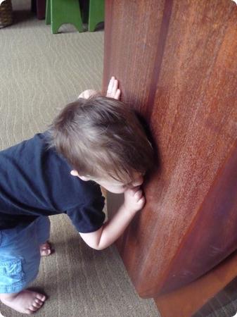 Eilan peeks through a toddler height peephole in a wooden surfboard